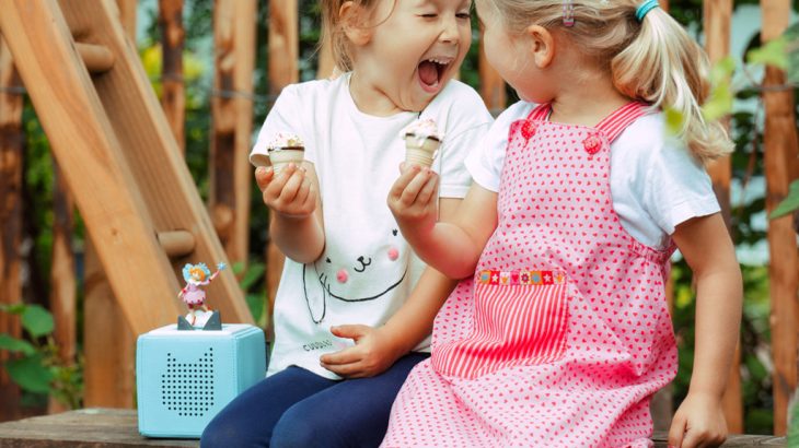 Zwei Kinder sitzen mit einer Toniebox im Garten. Foto zum Beitrag über Musikboxen